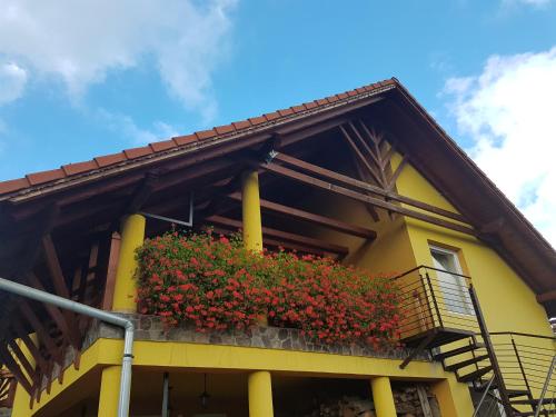 a yellow building with a balcony with red flowers at Hazanéző Panzió in Corund
