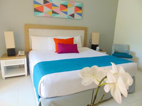a bedroom with a bed with colorful pillows and a flower at Casa Marina Beach & Reef All Inclusive in Sosúa