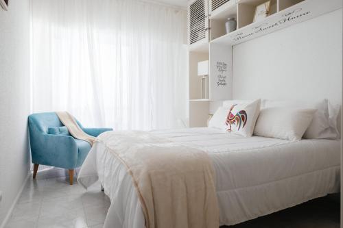 a white bedroom with a bed and a blue chair at 2 Room Condo - 5 mins from Costa da Caparica Beach & Bars in Costa da Caparica