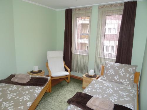 a bedroom with a bed and a chair and two windows at Teleki Apartman Kaposvár in Kaposvár
