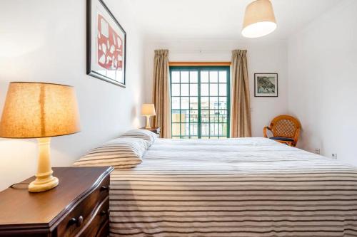 a bedroom with a bed with a lamp and a window at Apartamento Parque Ria Formosa, Olhão in Olhão
