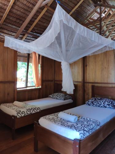 two beds in a room with a mosquito net at Harmony Bay Resort and Dive Center in Wakai