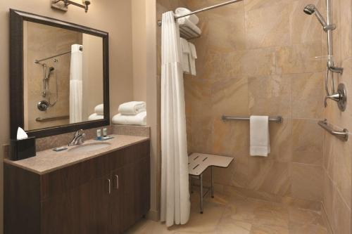 a bathroom with a shower and a sink and a mirror at Hyatt House Minot- North Dakota in Minot