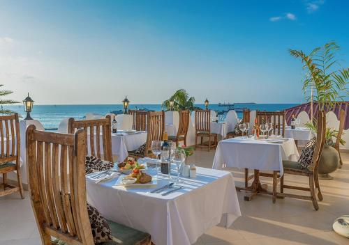 a restaurant with tables and chairs with the ocean in the background at The Seyyida Hotel and Spa in Zanzibar City