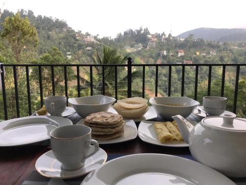 a table with cups and plates of food on a balcony at Rawana Rock Road Homestay in Ella