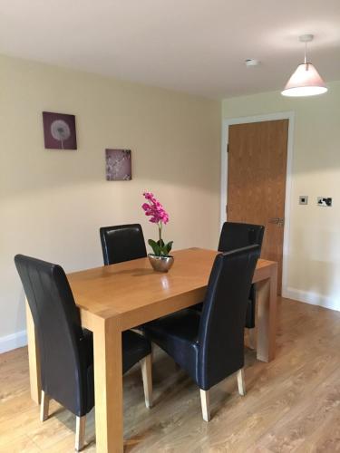 a wooden table with black chairs and a vase with flowers on it at Shannon Oaks Apartments in Portumna