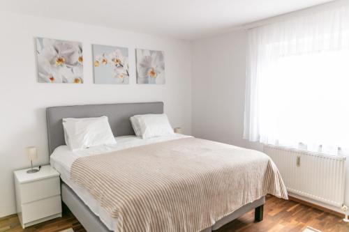 a white bedroom with a bed and two paintings on the wall at KRACHER Familienapartment mit Nationalparkblick in Illmitz
