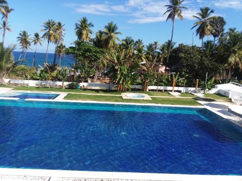 a swimming pool with palm trees and the ocean at Oasi Encantada - Beach Resort in Santa Cruz de Barahona