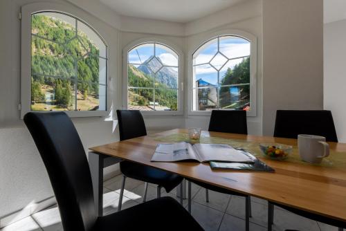 a dining room with a table and chairs and windows at Haus Piccolo in Saas-Grund