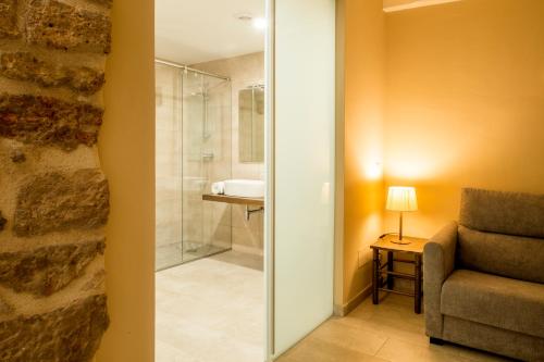 uma casa de banho com uma cabina de duche em vidro e uma cadeira. em Habitacions Plaça Major em Santa Pau