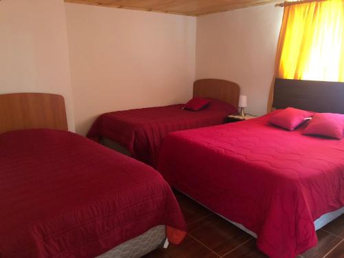 two beds in a room with red sheets at Hostería Estelita in Panimávida