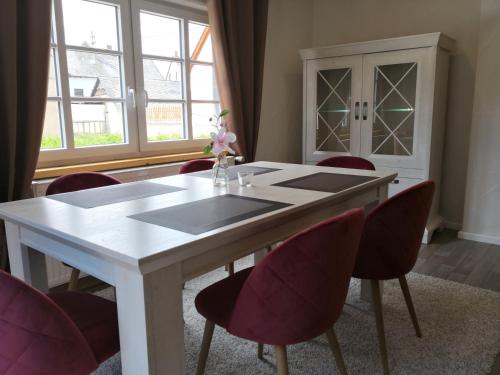 a dining room with a white table and red chairs at Maifeld-Fewo Sonnenschein in Kerben