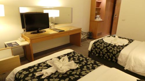 a hotel room with two beds and a desk with a television at Amman Airport Hotel in Al Qasţal