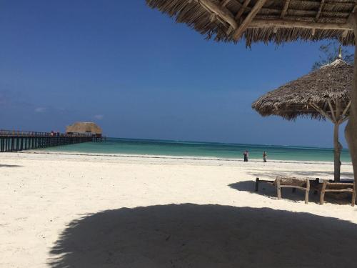 a beach with a straw umbrella and the ocean at Maisha Marefu Apartments in Kiwengwa
