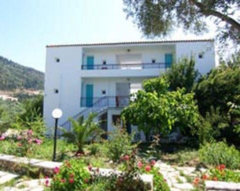 a white building with a balcony in a garden at Santa Maria Rooms in Agios Nikitas