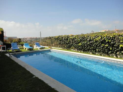 a swimming pool with two chairs and a hedge at Villa São Filipe in Baleia
