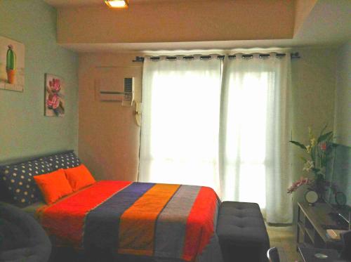 a bedroom with a bed with a colorful blanket and a window at Studio Fully Furnished in Manila
