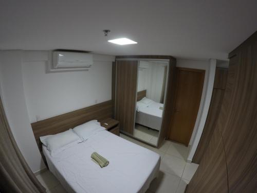 um pequeno quarto com uma cama branca e um espelho em Flat no Brookfield Towers em Goiânia