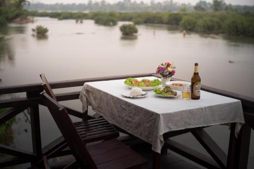 Ban Khon的住宿－Chanhthida Riverside Guesthouse and The River Front Restaurant，一张桌子,上面放着两盘食物和一瓶葡萄酒