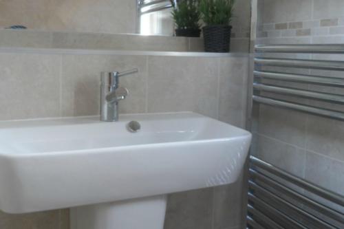 a white sink in a white tiled bathroom at Knightcote Farm Cottages in Gaydon