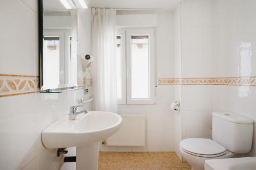 a white bathroom with a toilet and a sink at Hotel El Cid in Morella