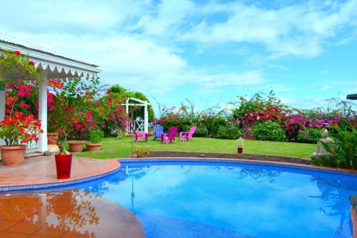 a swimming pool in a yard with pink chairs and flowers at Villa Tangara - Faa'a - Tahiti - 3 bedrooms - pool and lagon view - 6 pers in Faaa