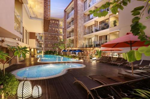 an outdoor swimming pool in a building with chairs and umbrellas at Harper Kuta Hotel by ASTON in Legian