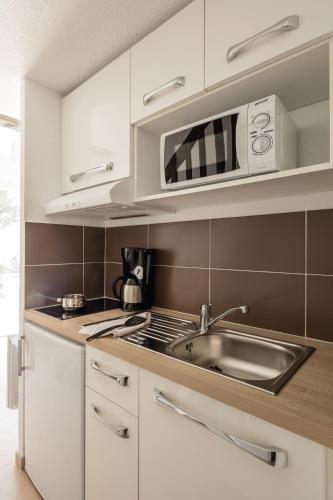 a white kitchen with a sink and a microwave at Comfort Aparthotel Mandelieu la Napoule Village in Mandelieu-la-Napoule
