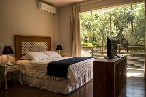 a bedroom with a bed and a television and a window at Pousada Recanto das Araras in Tiradentes