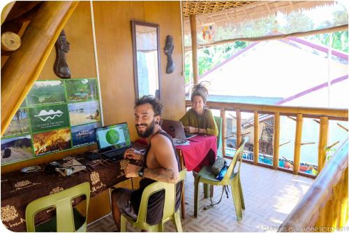 a man sitting at a desk with a computer at Darpins Guesthouse in Dauin