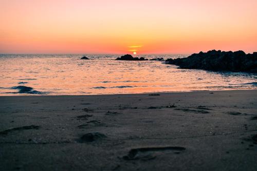 a sunset on a beach with the ocean and rocks at Horizon Eco Resort in Ko Phra Thong