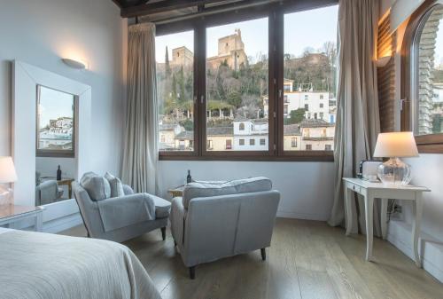 a bedroom with a bed and two chairs and a large window at Shine Albayzín in Granada