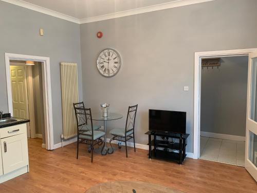 a living room with a table and a clock on the wall at The Snug Garden Apartment in Llandudno