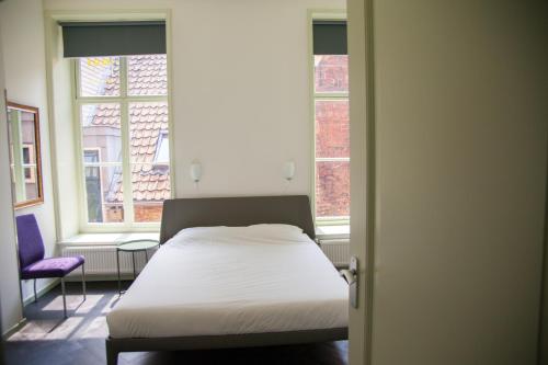 a bed in a room with two windows at Gelkingehof Aparthotel in Groningen