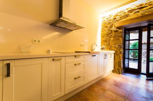 a kitchen with white cabinets and a stone wall at Casa Rural La Villa de Tábara in Tábara
