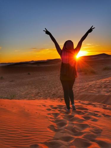 a woman is standing in the desert with her arms up at Camp Sahara Holidays in Mhamid