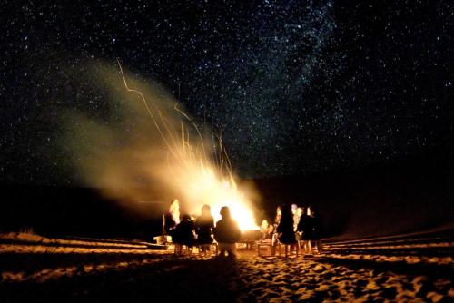 a group of people standing around a fire at night at Camp Sahara Holidays in Mhamid