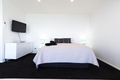 a white bedroom with a bed and a tv at Aqua-Heights Apartment in Nelson