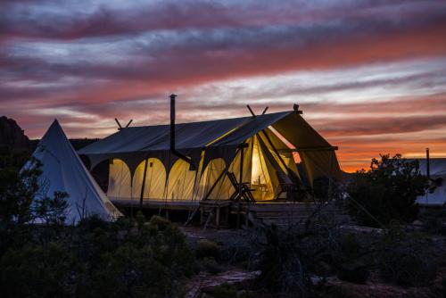 a tent in the middle of a field at sunset at Under Canvas Moab in Moab