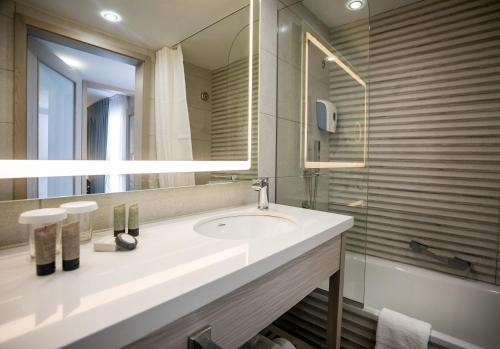 a bathroom with a sink and a mirror and a tub at Astral Village Hotel in Eilat