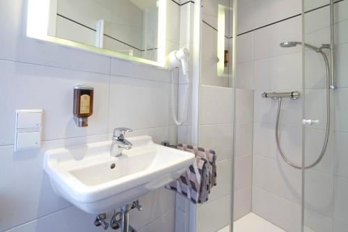 ein weißes Bad mit einem Waschbecken und einer Dusche in der Unterkunft Gästehaus Hebinger am Schlosspark in Deidesheim