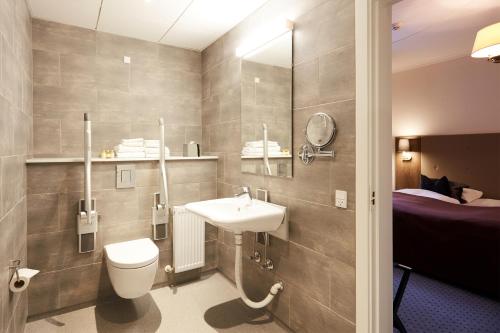 a bathroom with a sink and a toilet and a bed at Hotel Vejlefjord in Stouby
