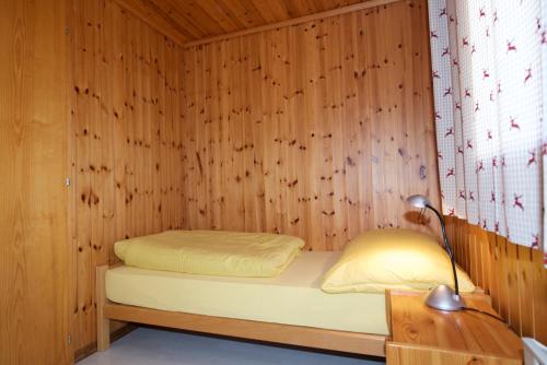 Cama pequeña en habitación de madera con lámpara en Apartment Alouette Riederalp, en Riederalp