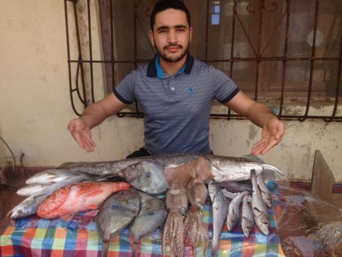 un homme debout à côté d'un tas de poissons dans l'établissement Hotel El ghazi, à Tarfaya