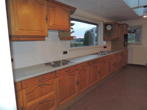 an empty kitchen with wooden cabinets and a window at Vakantiehuis " Te Lande " in Torhout