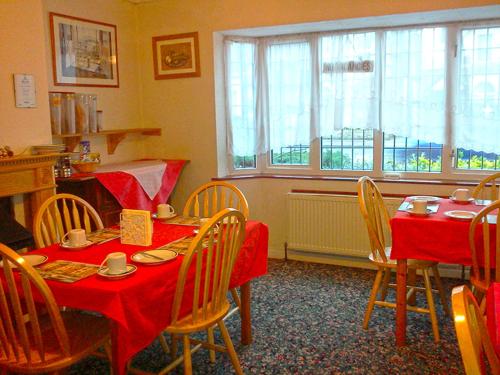 een eetkamer met 2 tafels en stoelen met rode tafellakens bij Carlton Lodge in Cambridge