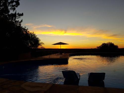 a sunset with an umbrella and two chairs and a pool at Al Kamar Cabañas Lodge in Santa Ana