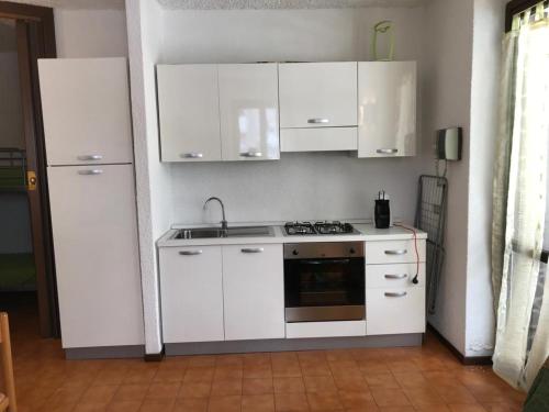 una cucina con armadi bianchi, lavandino e piano cottura di Il Capriolo a Piazzatorre