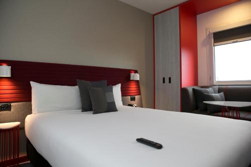a bedroom with a large white bed with a remote control on it at ibis Sydney Airport in Sydney