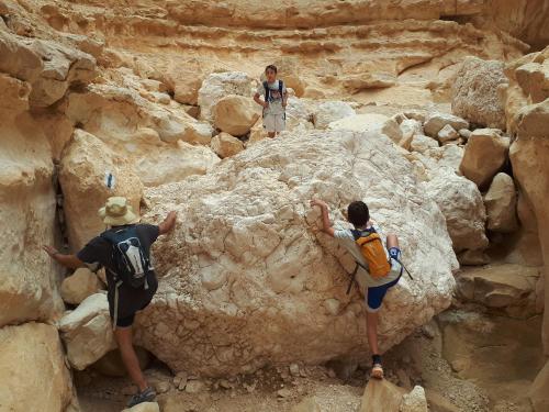 three people climbing on rocks in a canyon at רגע ערבה in ‘En Yahav
